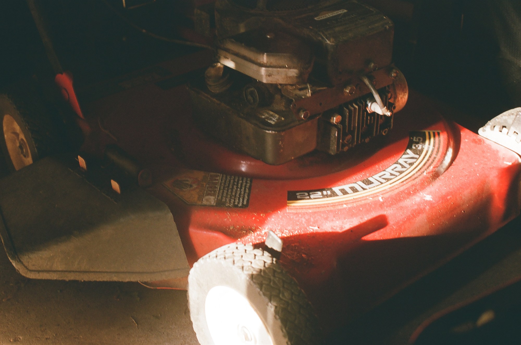 A red Murray mower in a dark shed, lit by hard sun